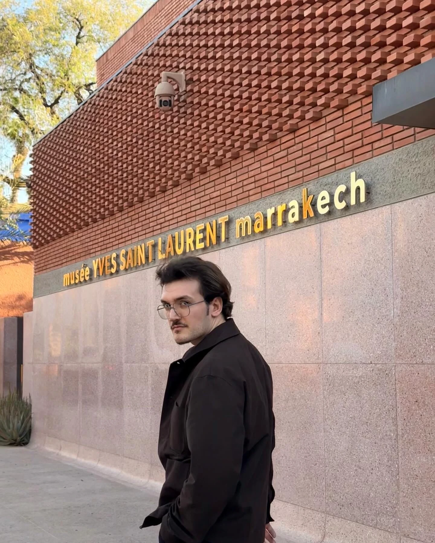 Standing outside the Musée Yves Saint Laurent in Marrakech, the building’s brick facade behind